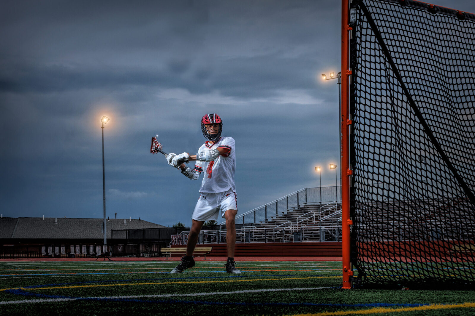 High school senior practicing a lacrosse shot into the net during a dramatic nighttime senior portrait session.