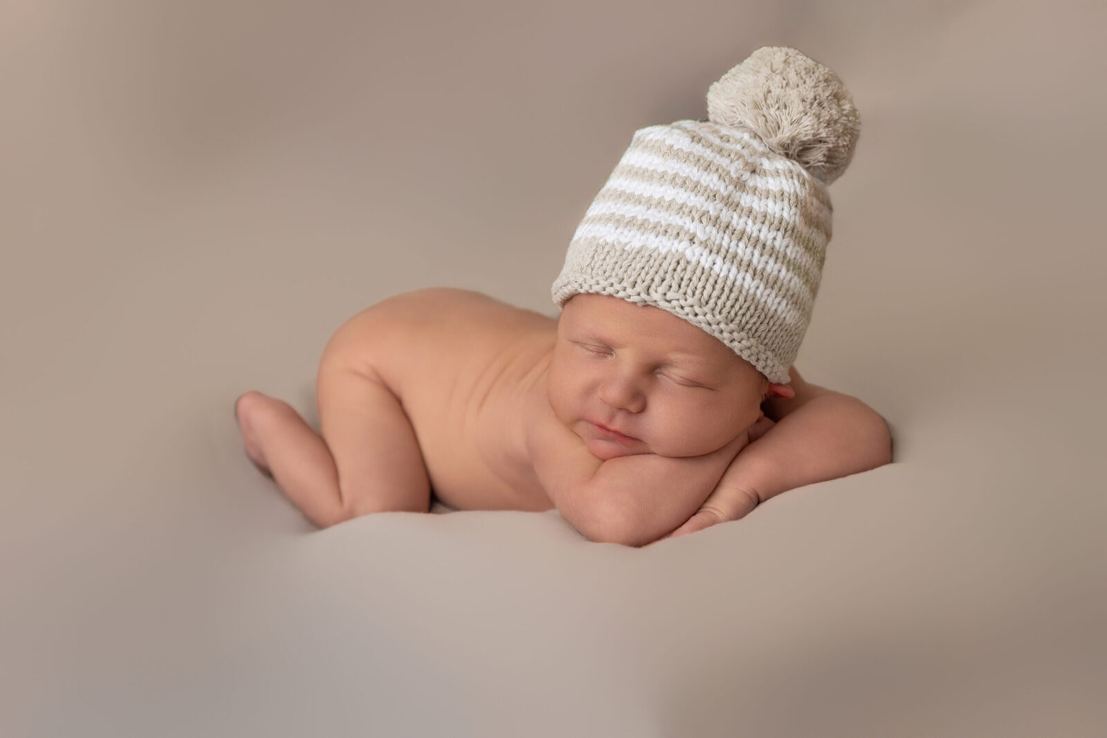 Sleeping newborn baby wearing a tan and white knit beanie during a cozy professional newborn photography session.